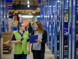 Two workers walking a warehouse aisle lined with stock