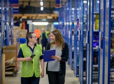 Two workers walking a warehouse aisle lined with stock