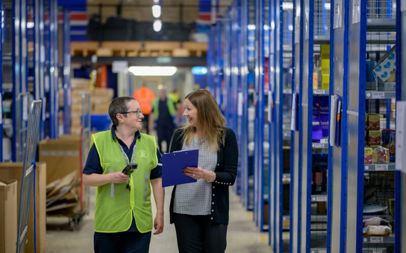Two workers walking a warehouse aisle lined with stock