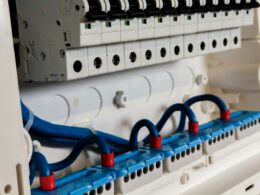 Open electrical panel showing a row of circuit breakers above blue wiring