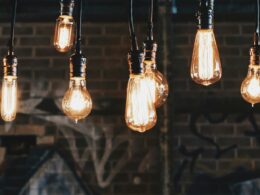 Rows of glowing filament light bulbs hanging on cords in front of a dark brick wall