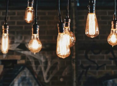 Rows of glowing filament light bulbs hanging on cords in front of a dark brick wall