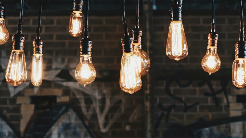 Rows of glowing filament light bulbs hanging on cords in front of a dark brick wall