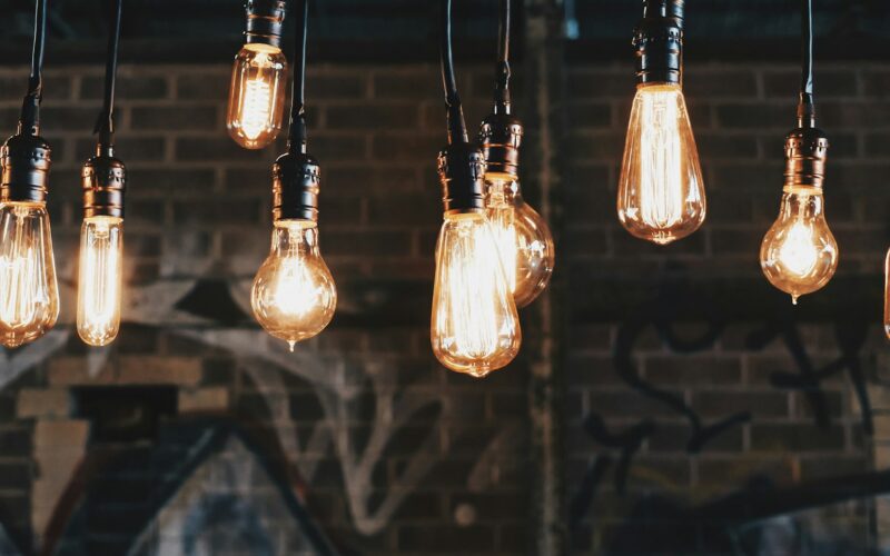 Rows of glowing filament light bulbs hanging on cords in front of a dark brick wall