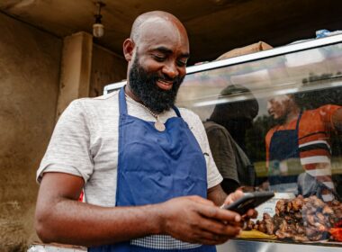 Food vendor at a street stall checking a smartphone between customers