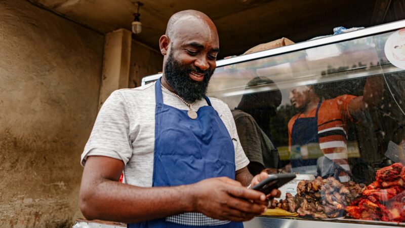 Food vendor at a street stall checking a smartphone between customers