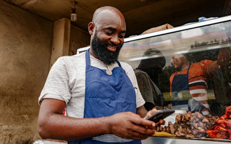Food vendor at a street stall checking a smartphone between customers