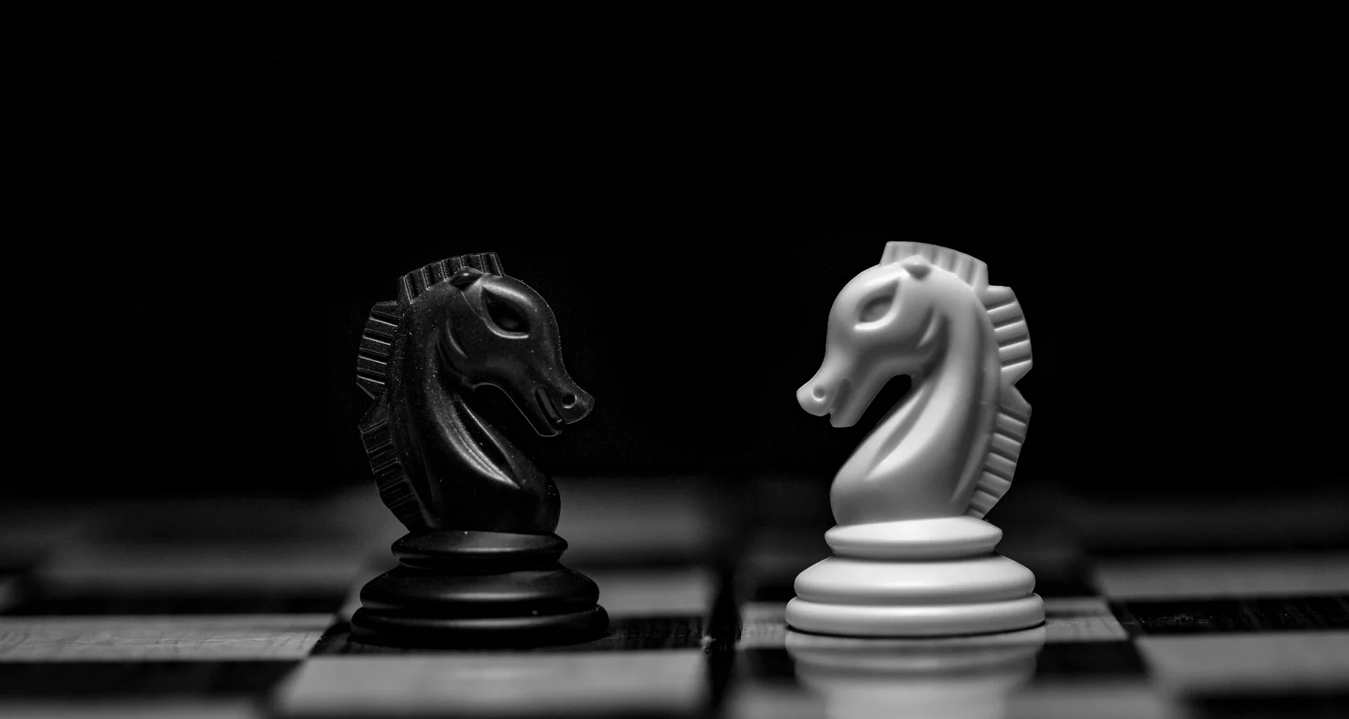 A black and a white chess knight facing each other on a board