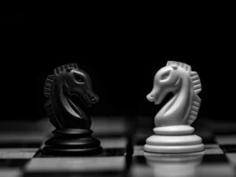 A black and a white chess knight facing each other on a board