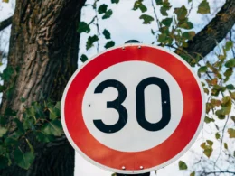 A red and white speed limit sign next to a tree