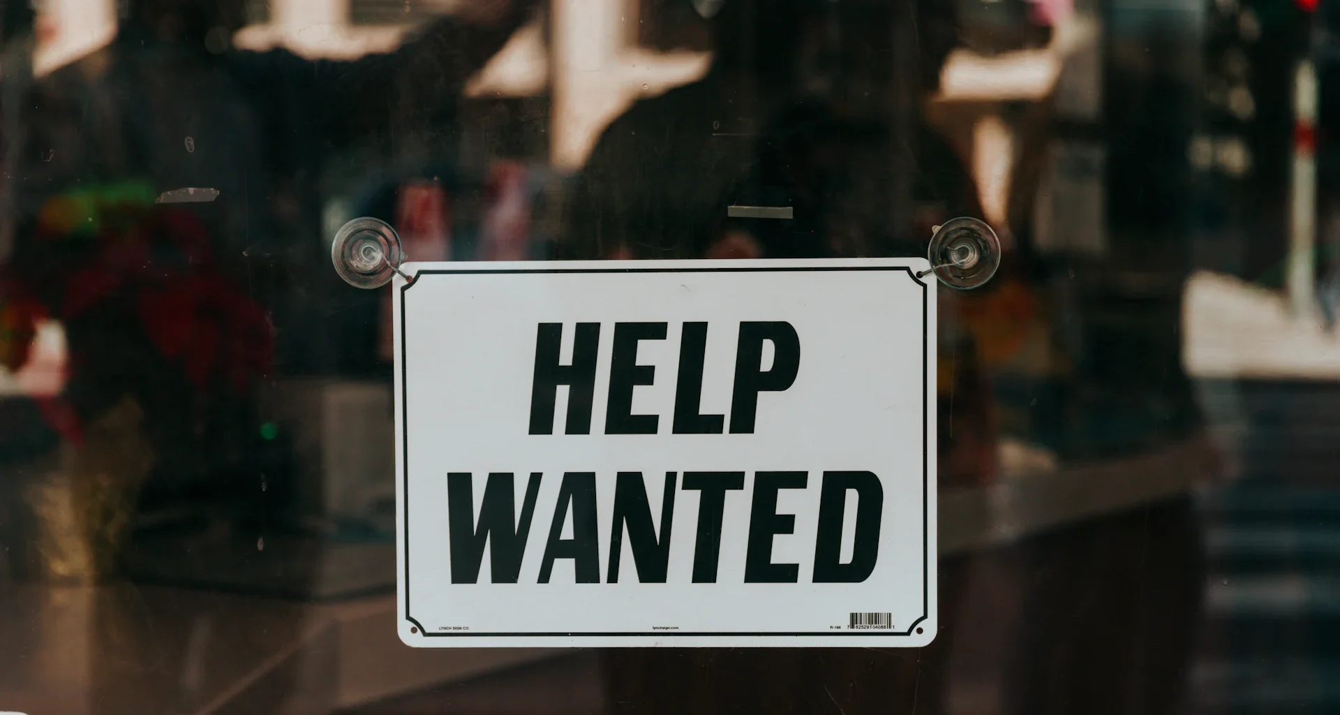 A sign that says help wanted on a glass door