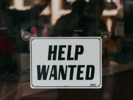 A sign that says help wanted on a glass door