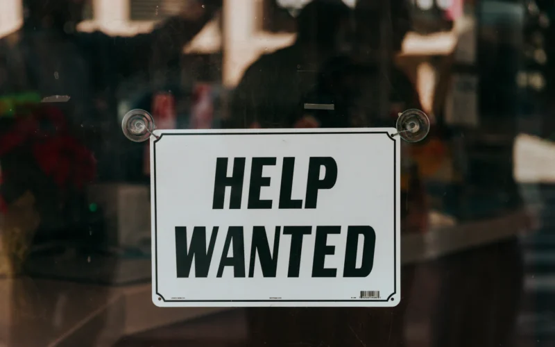 A sign that says help wanted on a glass door