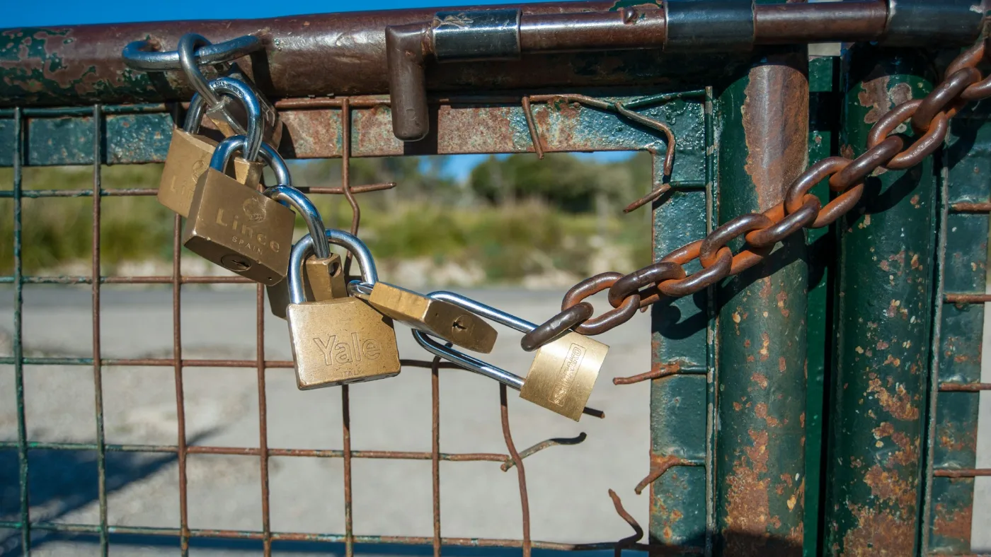 AI agent controls: brass padlock hanging on a bright blue metal fence.