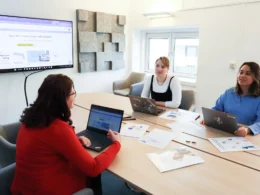 Three marketers at a meeting table with laptops and printed charts, testing AI marketing tools in Canada