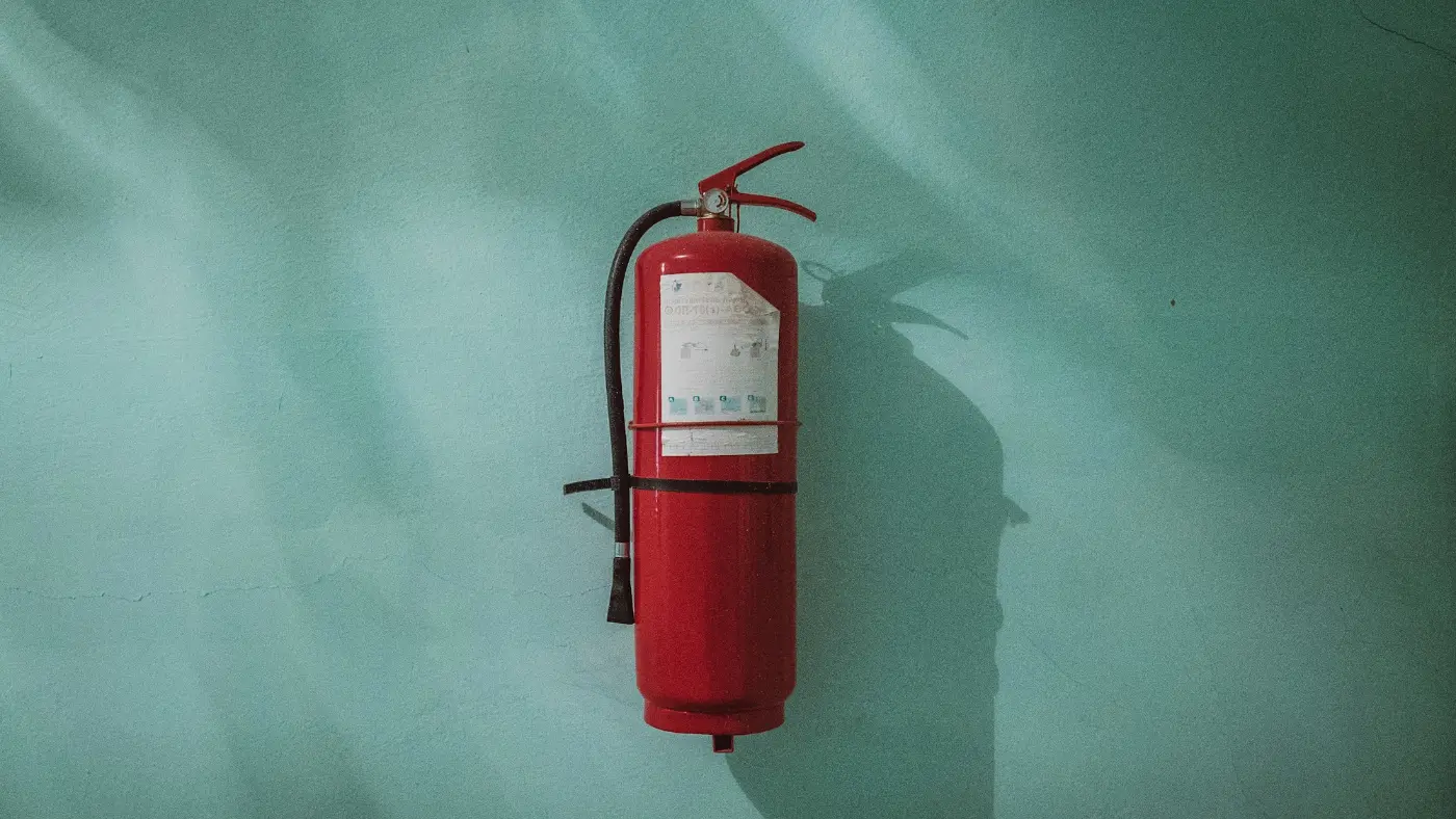 Red fire extinguisher mounted on a green wall.