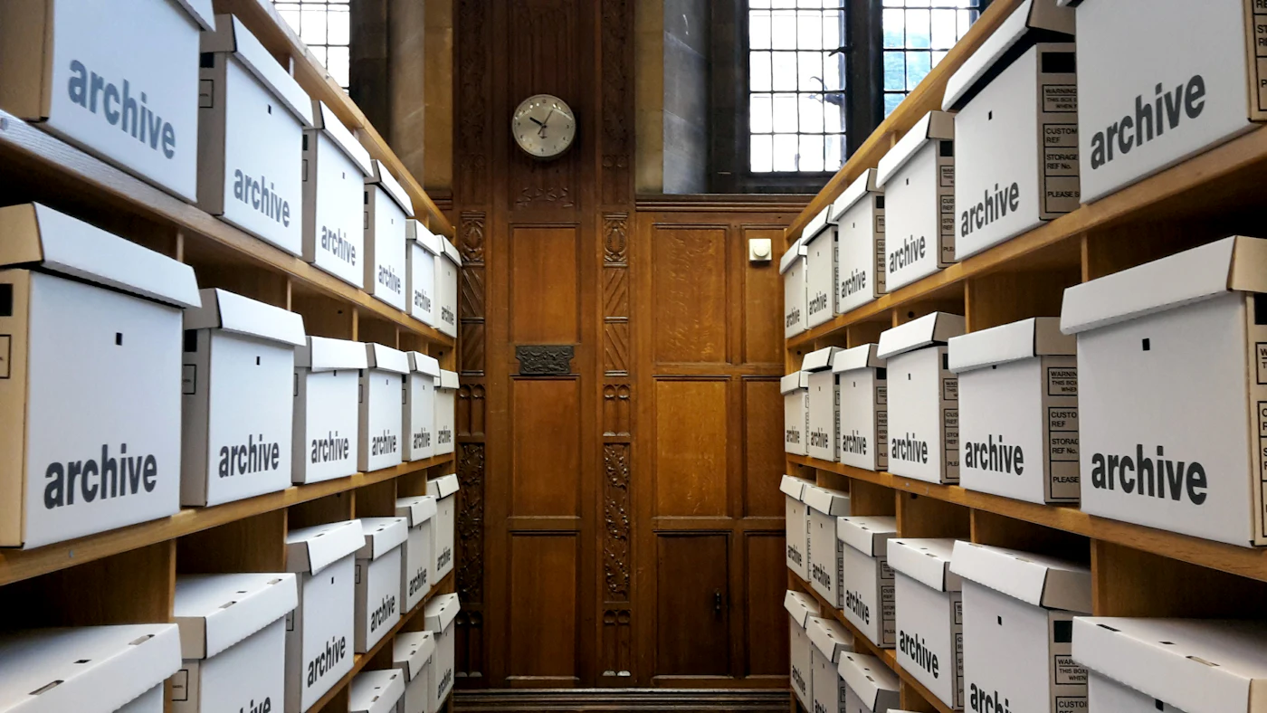 Rows of white archive boxes on wooden shelves in a records room