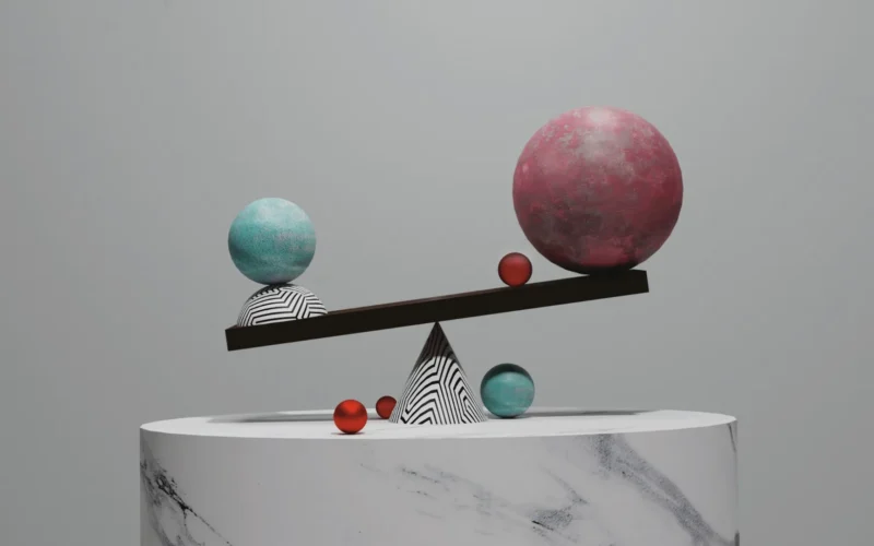 A balance scale with two spheres on a marble pedestal against a grey background