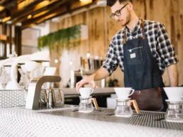 A young barista in an apron working behind a cafe counter