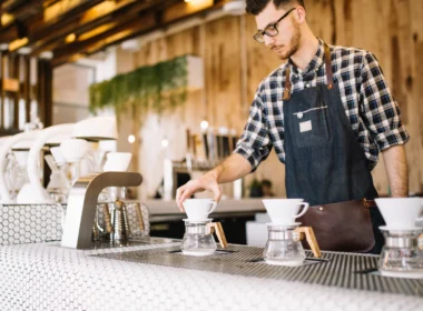 A young barista in an apron working behind a cafe counter