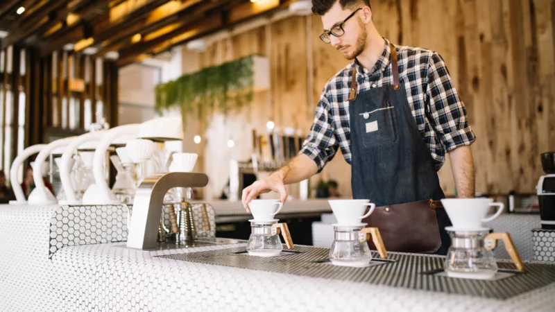 A young barista in an apron working behind a cafe counter