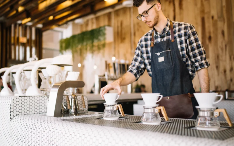 A young barista in an apron working behind a cafe counter