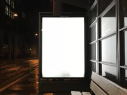 Blank glowing billboard at a wet bus stop at night