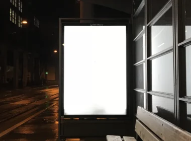 Blank glowing billboard at a wet bus stop at night