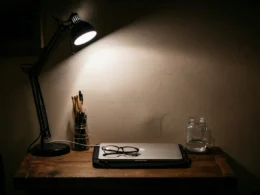 A black desk lamp glowing on a wooden table in a dark room