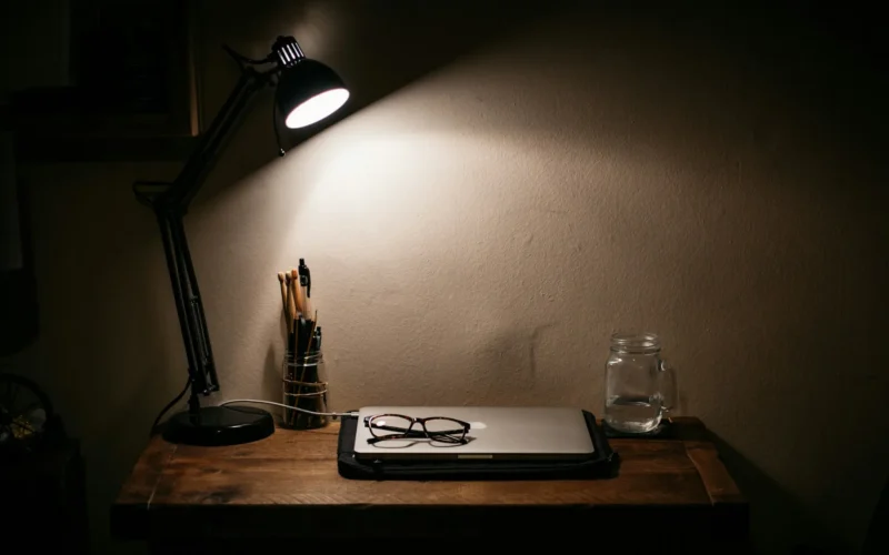 A black desk lamp glowing on a wooden table in a dark room