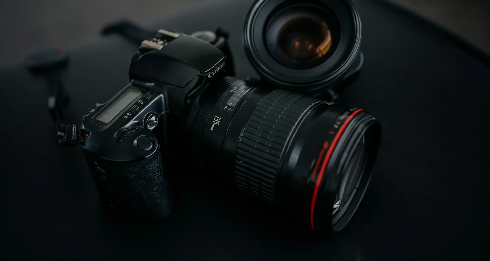 A black DSLR camera resting beside a camera lens