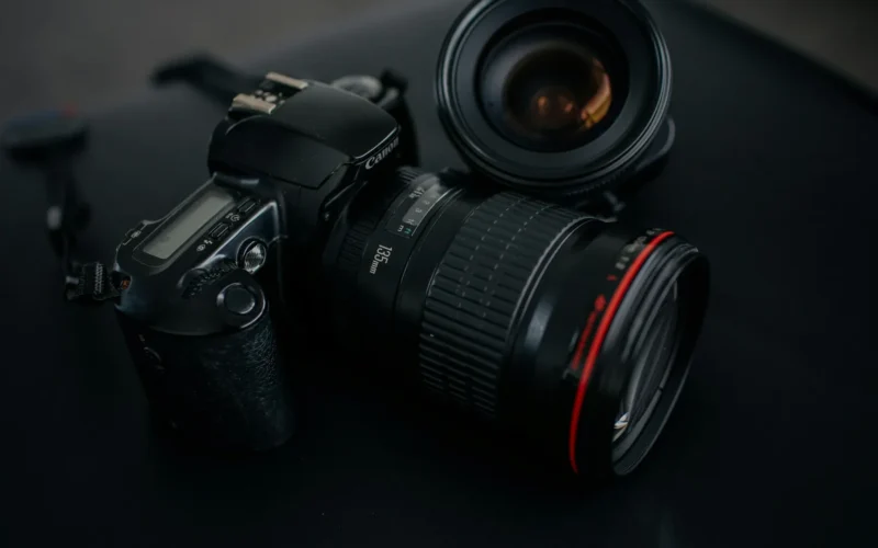 A black DSLR camera resting beside a camera lens