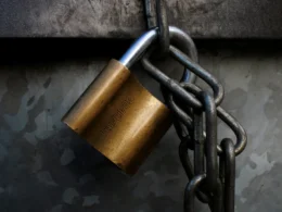 A brass padlock hanging from a grey metal chain