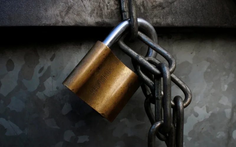 A brass padlock hanging from a grey metal chain
