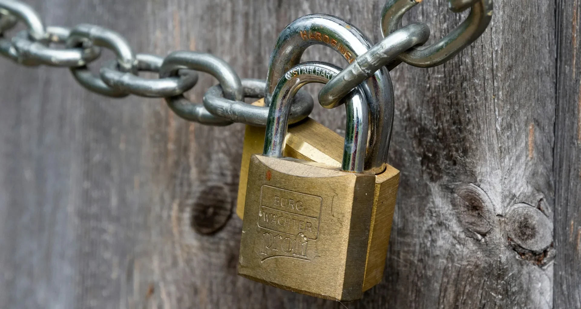 A brown padlock fixed to a weathered wooden fence