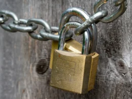 A brown padlock fixed to a weathered wooden fence