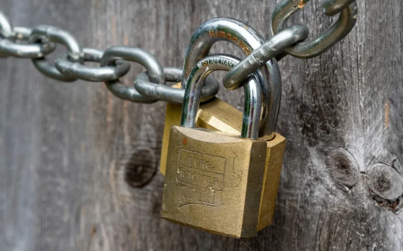 A brown padlock fixed to a weathered wooden fence