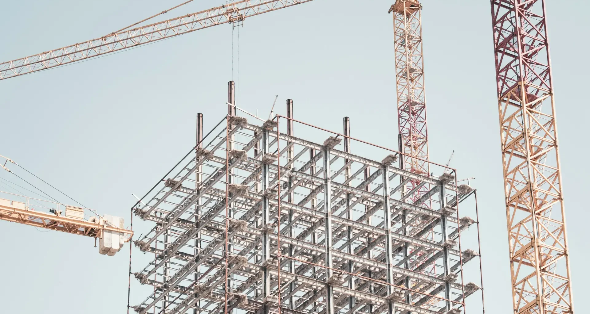 Gray metal building frame beside a tower crane during the day