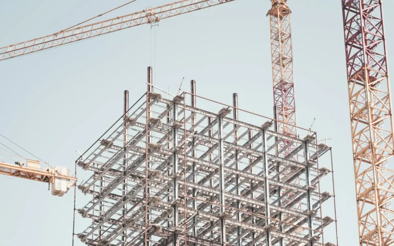 Gray metal building frame beside a tower crane during the day
