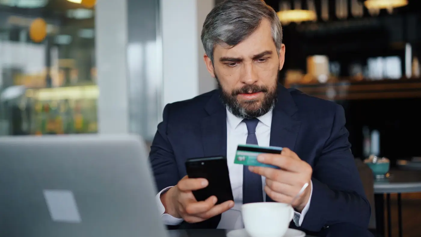 Business owner checking a phone and bank card, the kind of account third-party AI agents can no longer reach
