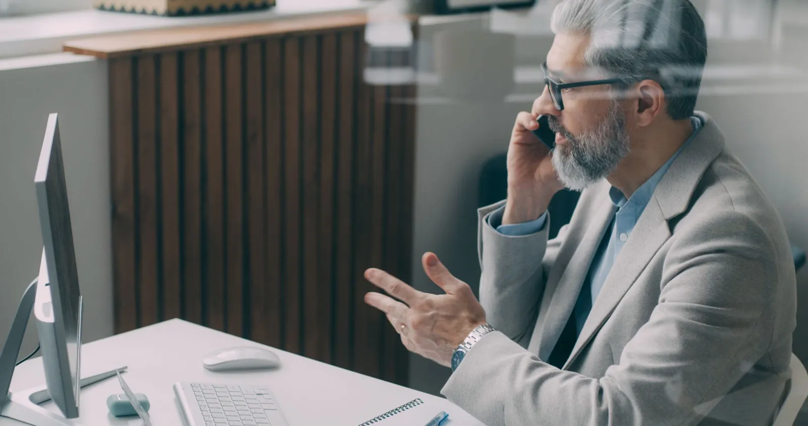 Siri AI French support: senior businessman on a phone call at his desk in a modern office.