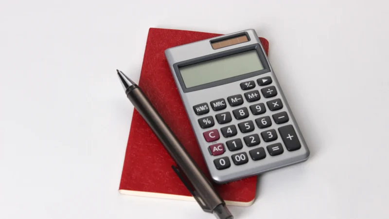 Silver calculator and black pen resting on a red notebook against a white background