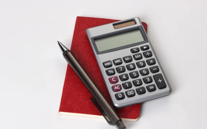 Silver calculator and black pen resting on a red notebook against a white background