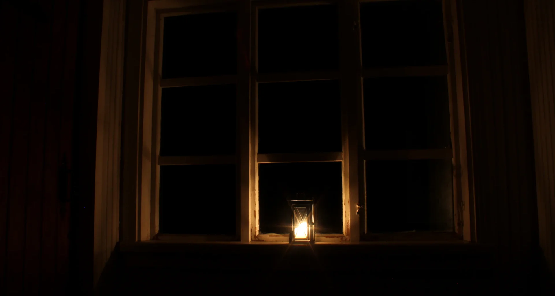 A lit candle in front of a window