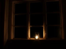 A lit candle in front of a window
