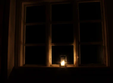 A lit candle in front of a window