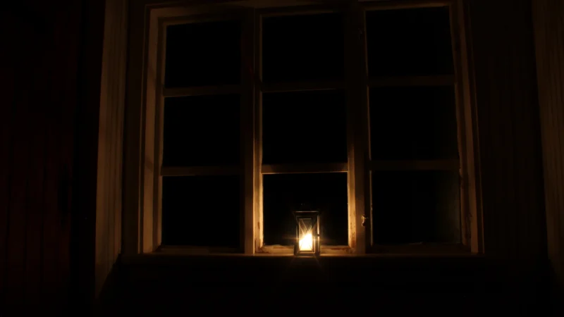 A lit candle in front of a window
