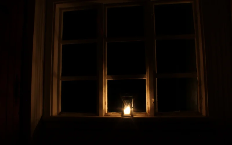 A lit candle in front of a window