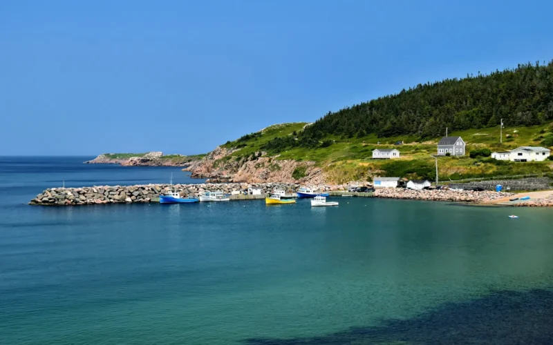Small harbour with fishing boats below green hills on the Cape Breton Island coast in Nova Scotia