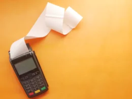Card payment terminal printing a long paper receipt on an orange surface.